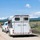 A horse inside of a horse trailer being pulled by a truck down a rural road