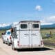 A horse inside of a horse trailer being pulled by a truck down a rural road